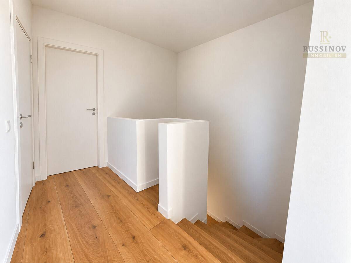 Heller Flur im Obergeschoss mit Holztreppe und weiß gestrichenen Wänden.