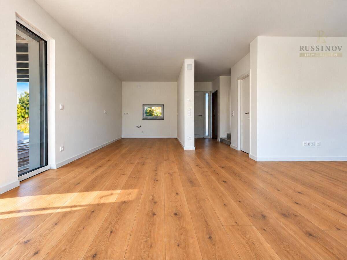 Geräumiger, heller Wohnbereich mit Holzboden und Zugang zu weiteren Räumen.