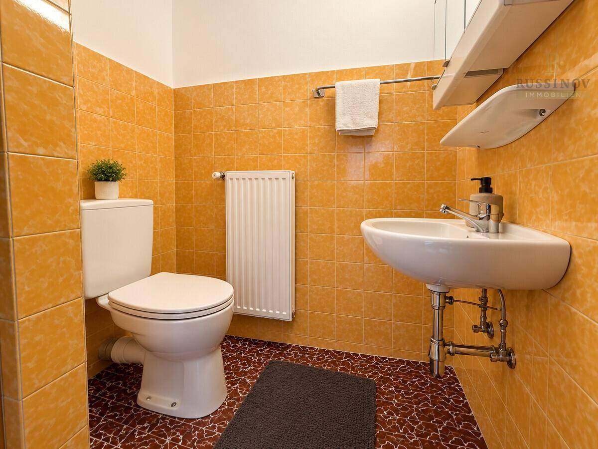 Helles Badezimmer mit WC, Waschbecken und orangefarbenen Wand- und Bodenfliesen.