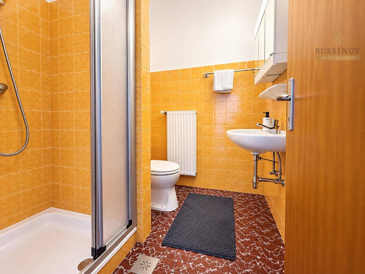 Funktionales Badezimmer mit Duschkabine, WC, Waschbecken und orangefarbenen Fliesen.