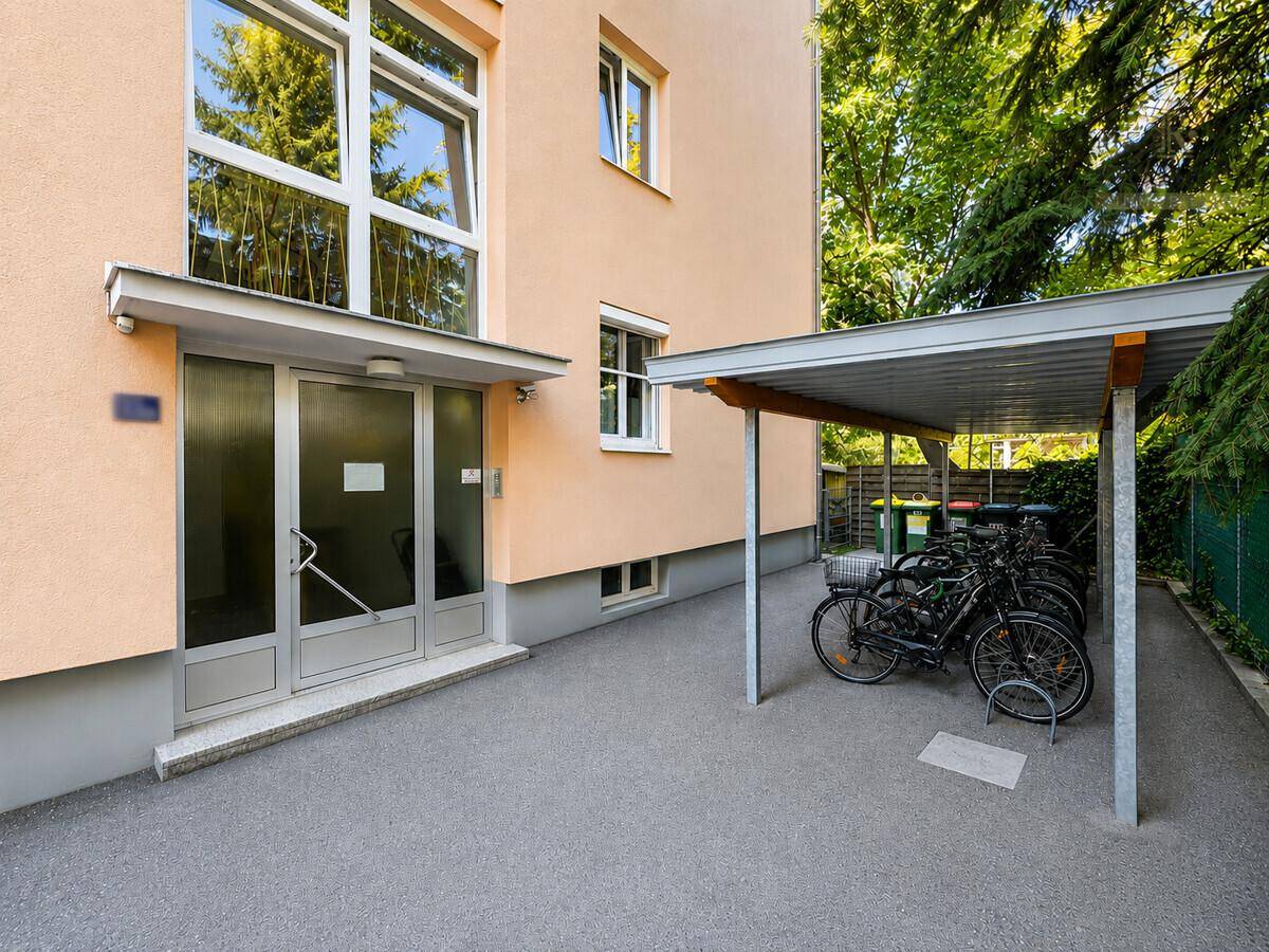 Eingangsbereich eines Mehrfamilienhauses mit Fahrradabstellplatz unter einem Carport.