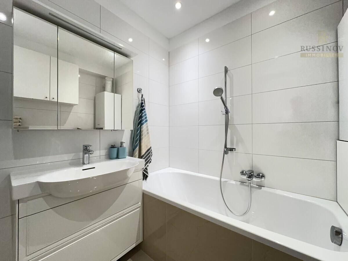 Modernes Badezimmer mit Badewanne, Waschtisch und Spiegelschrank, hell gefliest.