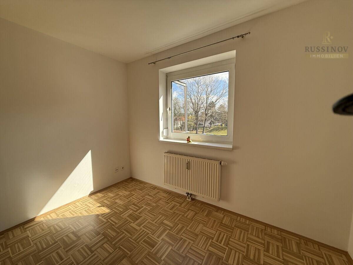 Helles Schlafzimmer mit Parkettboden und einem Fenster, das viel Tageslicht hereinlässt.