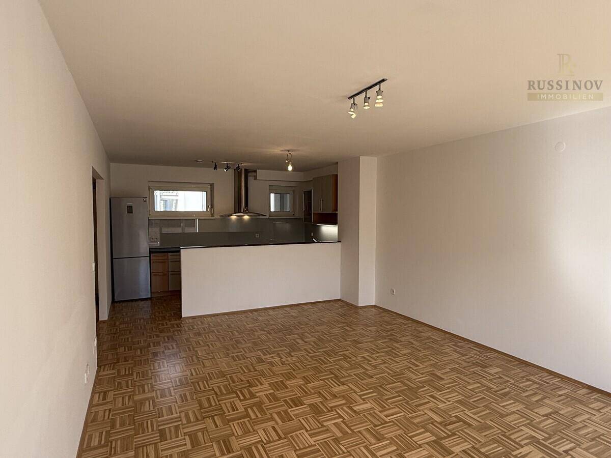 Geräumiger Wohnbereich mit Parkettboden und offener Verbindung zur Küche im Hintergrund.