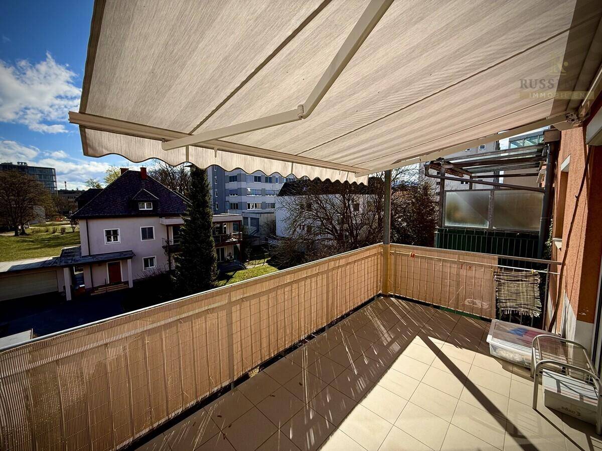 Überdachter Balkon mit Markise und Blick auf die umliegenden Gebäude und Grünflächen.