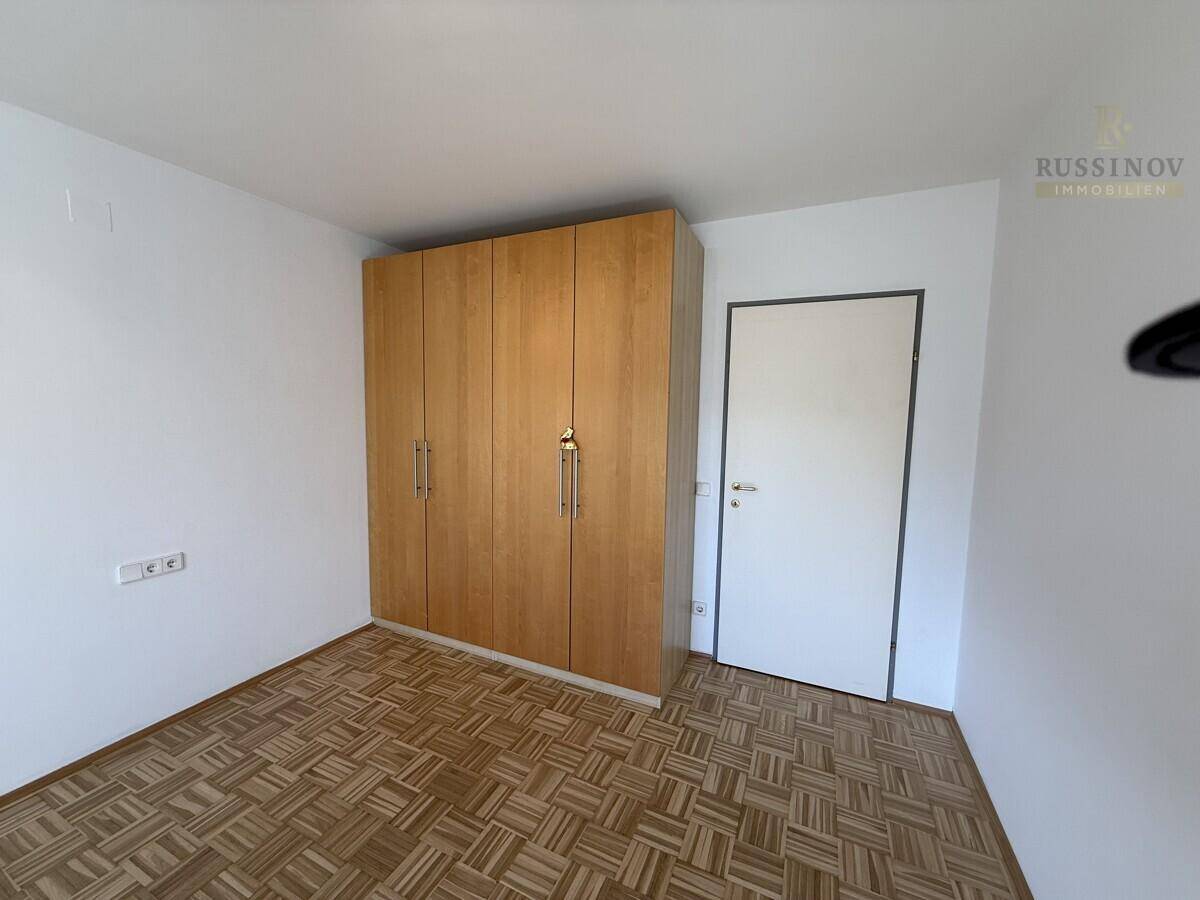 Schlafzimmer mit Parkettboden und einem großen Holzschrank, bietet viel Stauraum.