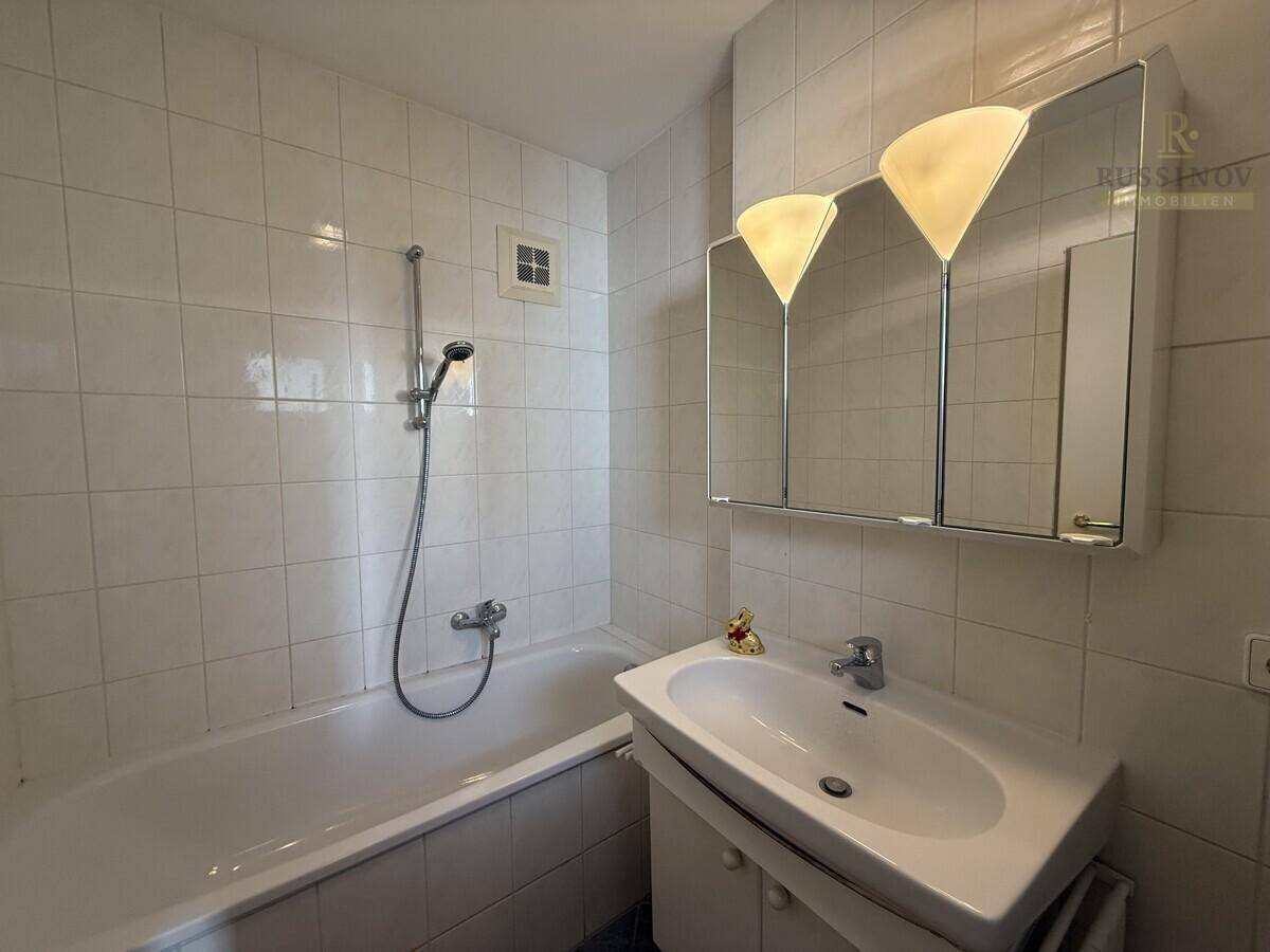 Gefliestes Badezimmer mit Badewanne, Waschbecken und Spiegelschrank, funktional eingerichtet.