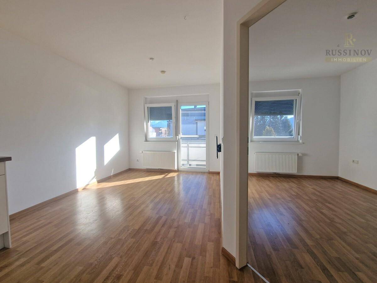 Heller Wohnbereich mit Holzboden und großen Fenstern, die viel Tageslicht hereinlassen.