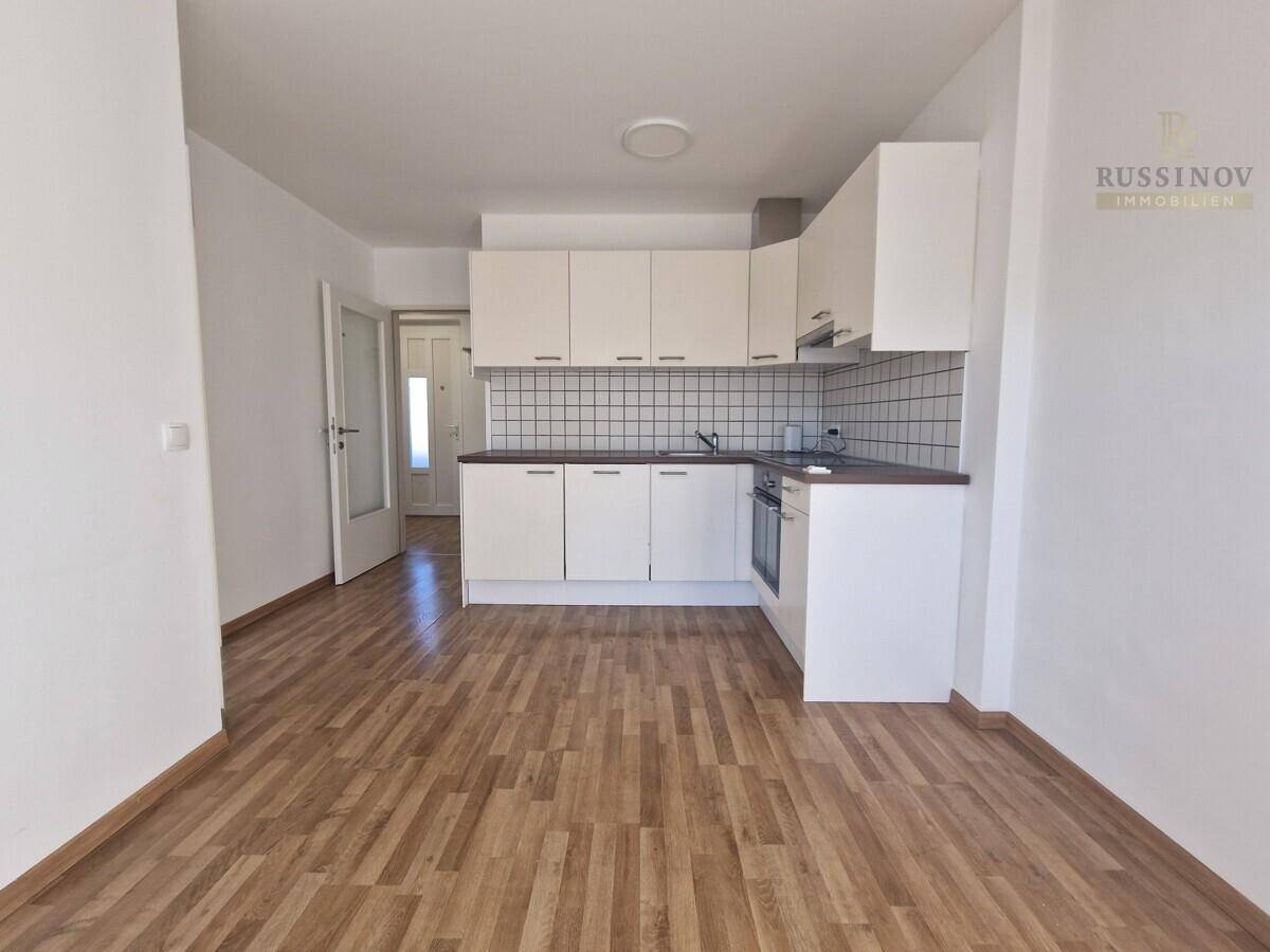 Offene Küche mit weißen Schränken, Fliesenrückwand und Holzboden, angrenzend an den Eingangsbereich.