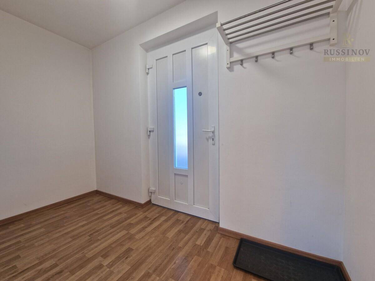 Eingangsbereich mit heller Holztür, Garderobe und Holzboden, einladend und funktional.