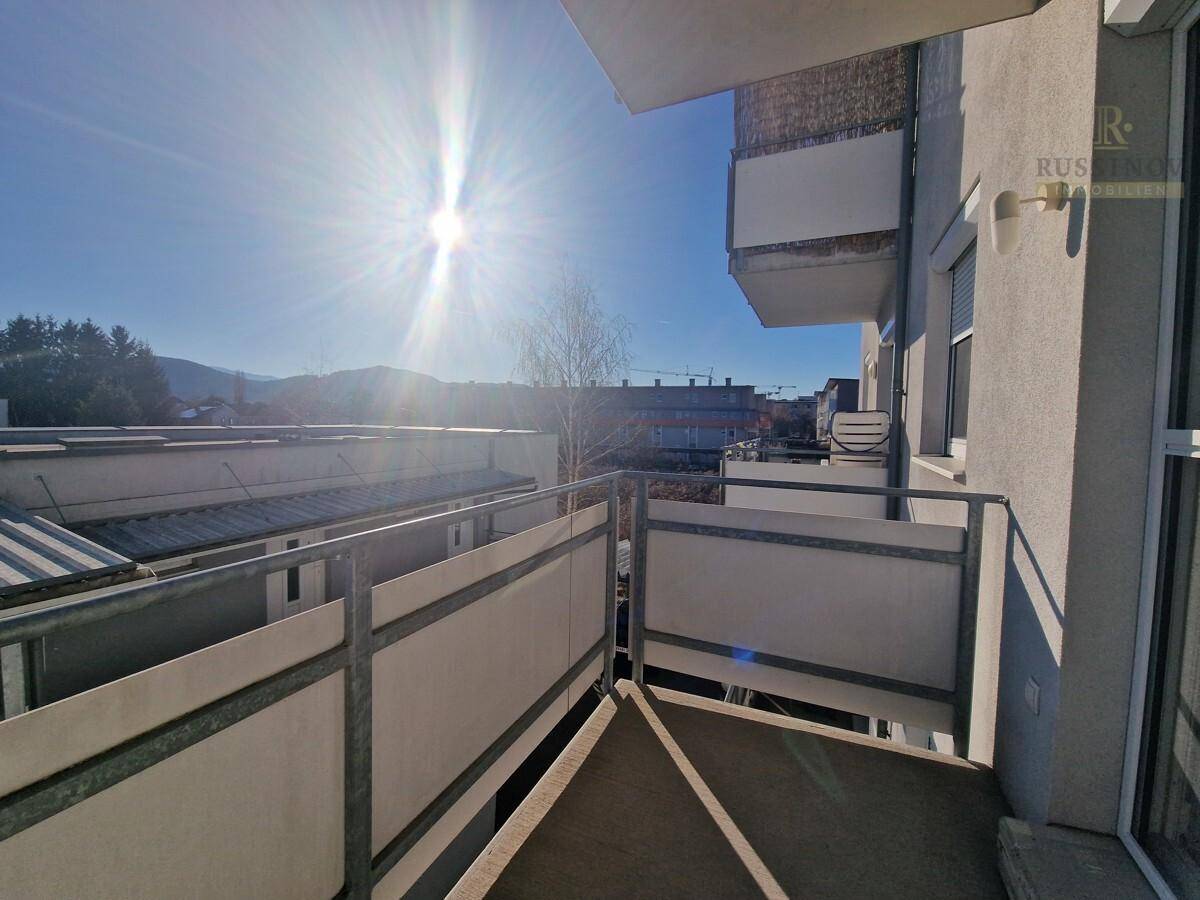 Sonniger Balkon mit Metallgeländer und weitem Blick über die Dächer der Umgebung.