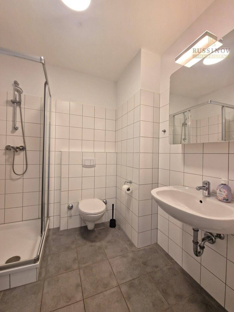 Modernes Badezimmer mit weißen Wandfliesen, Dusche, WC und Waschbecken, in gutem Zustand.