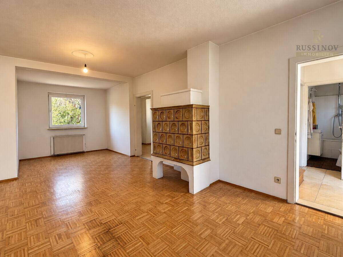 Geräumiges Wohnzimmer mit Parkettboden und traditionellem Kachelofen.
