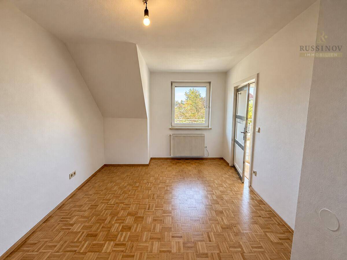 Schlafzimmer mit Parkettboden, Dachschräge und Zugang zu einem Balkon oder Terrasse.