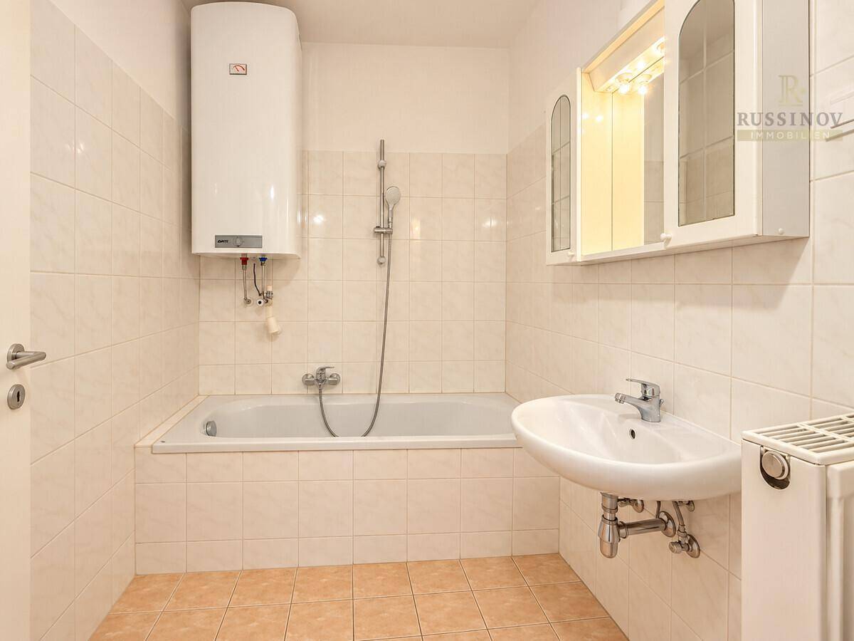 Funktionales Badezimmer mit Badewanne, Waschbecken und hellen Fliesen in neutralen Farbtönen.