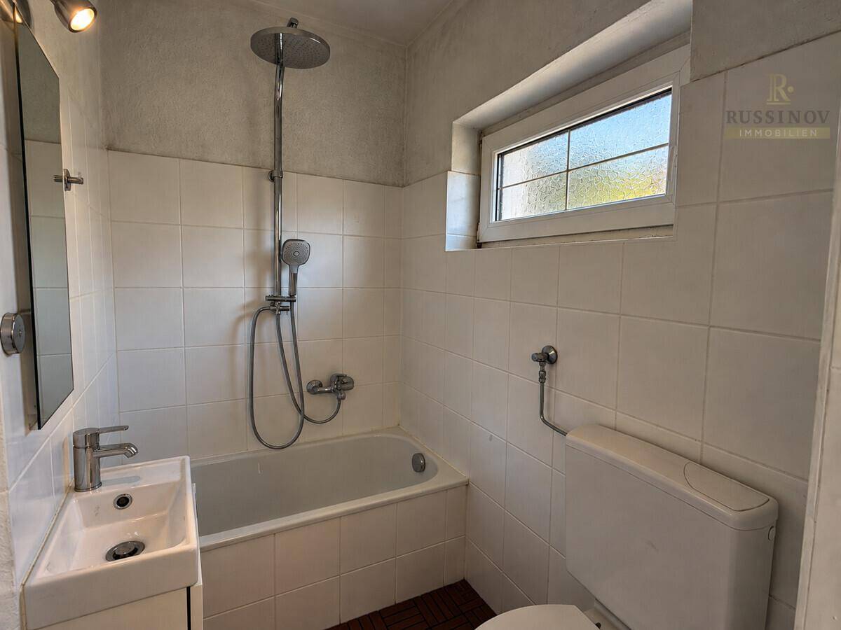 Gefliestes Badezimmer mit Badewanne, integrierter Dusche, Waschbecken und Fenster.