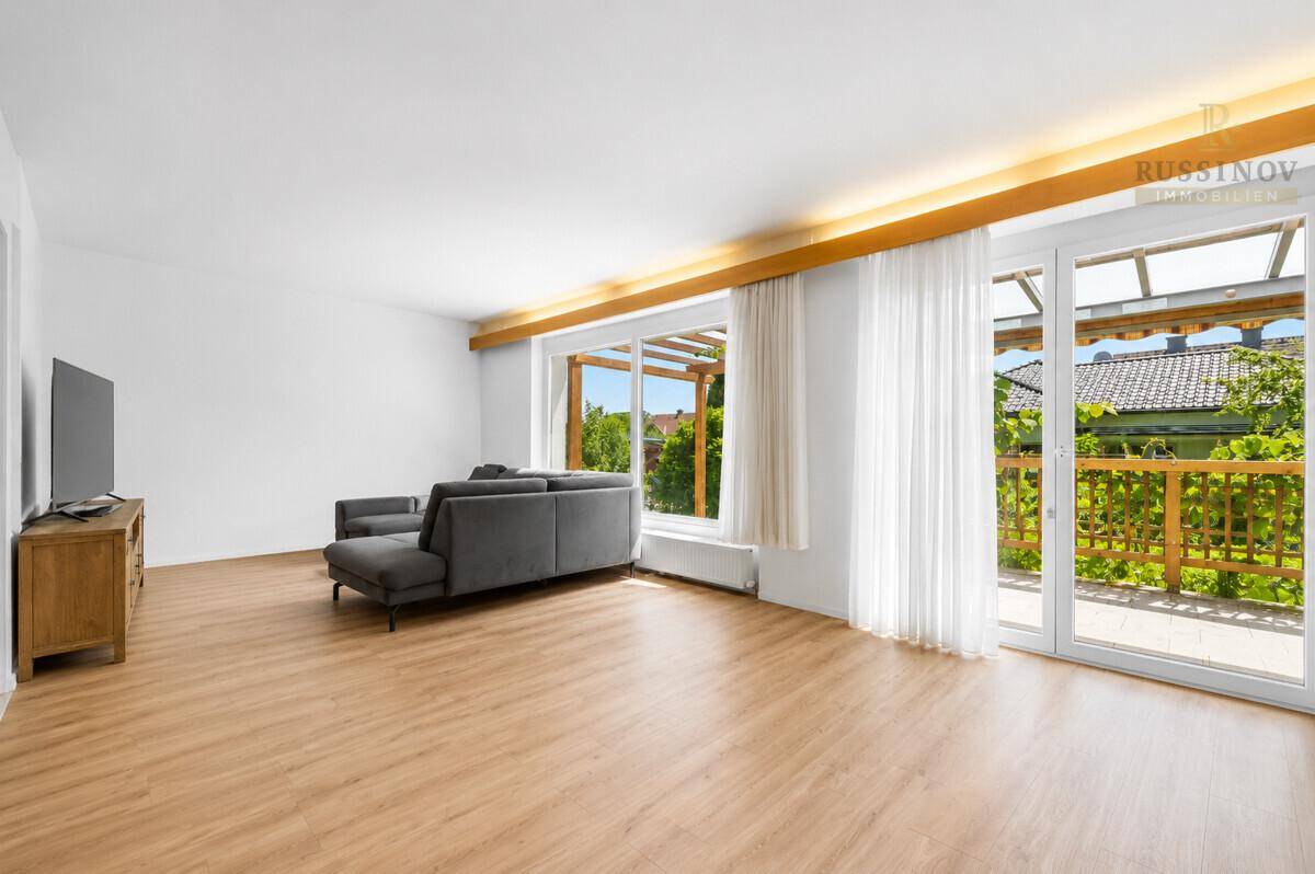 Helles und geräumiges Wohnzimmer mit Laminatboden, großen Fenstern und Zugang zum Balkon.