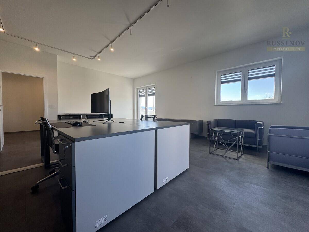 Großes Büro mit flexiblem Arbeitsbereich, bequemer Sitzecke und viel Tageslicht durch die Fenster.