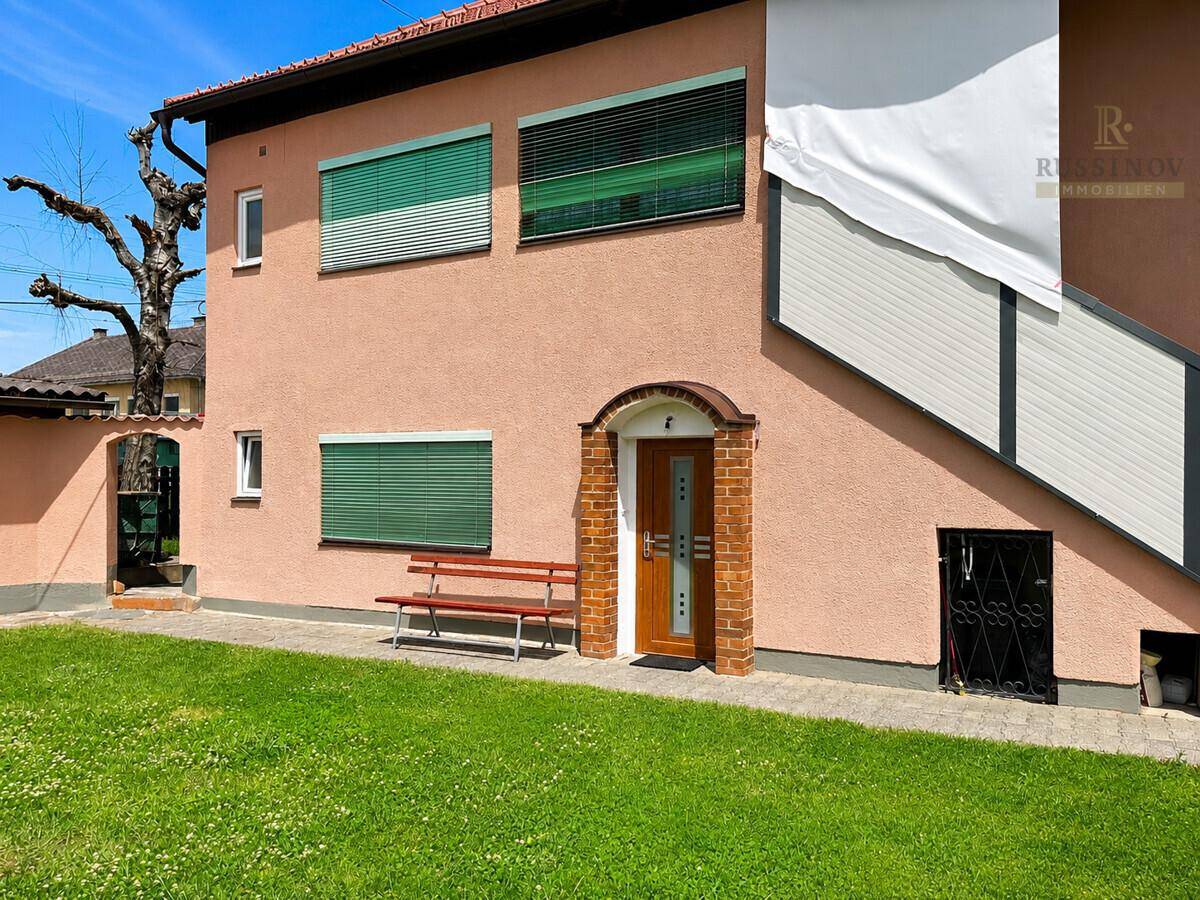 Eingangsbereich des Hauses mit Holztür, kleiner Bank und gepflegtem Rasen.