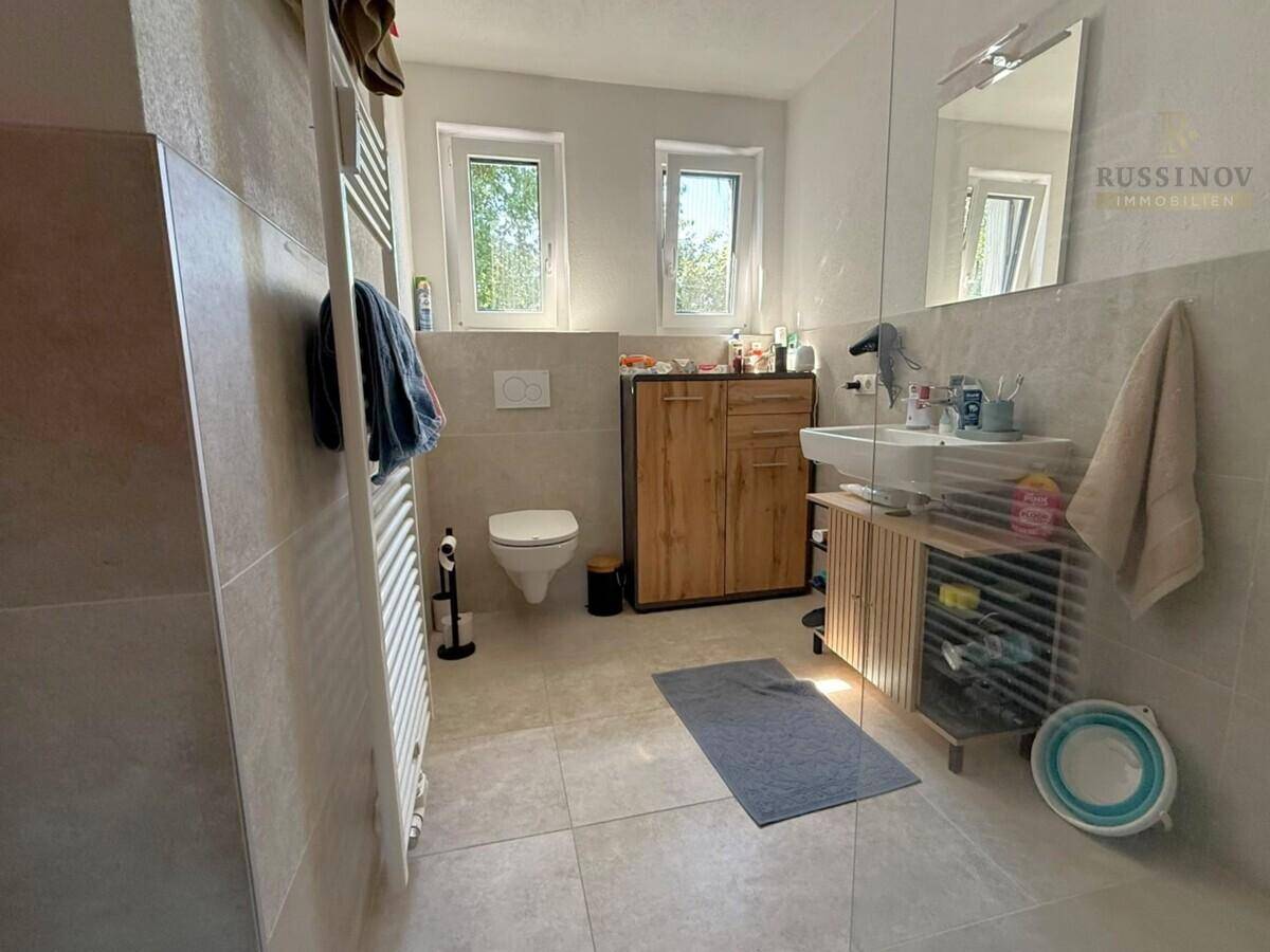 Modernes Badezimmer mit großen Fliesen, wandhängendem WC, Waschbecken und Fenster.