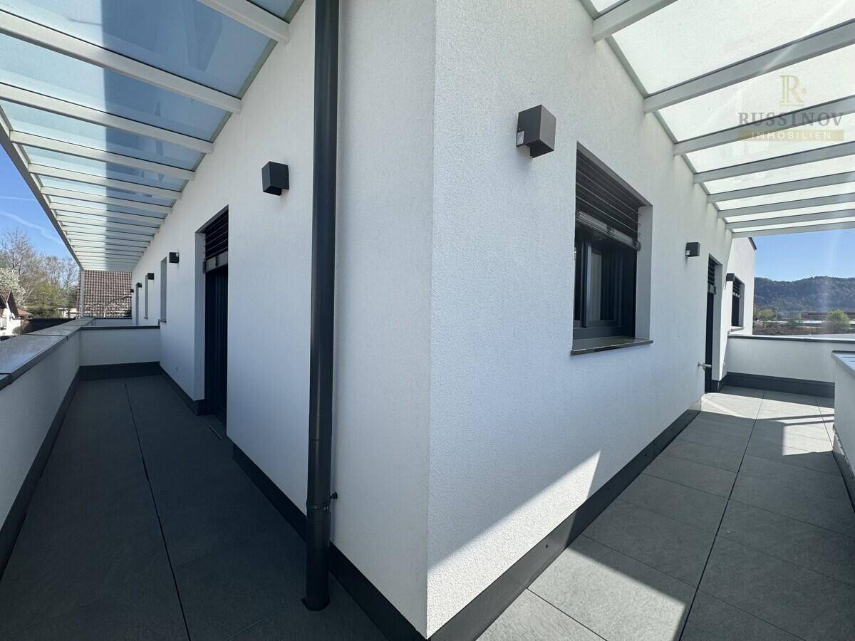 Langer, überdachter Balkon mit moderner Verglasung und weißer Fassade, ideal für entspannte Stunden.