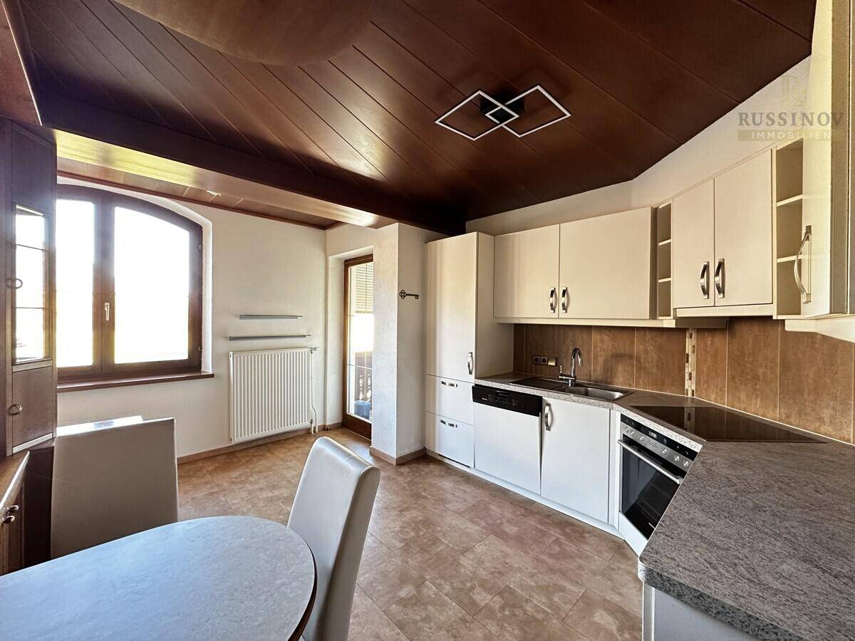 Helle Küche mit weißer Einbauküche, Essbereich und Zugang zu einem Balkon.