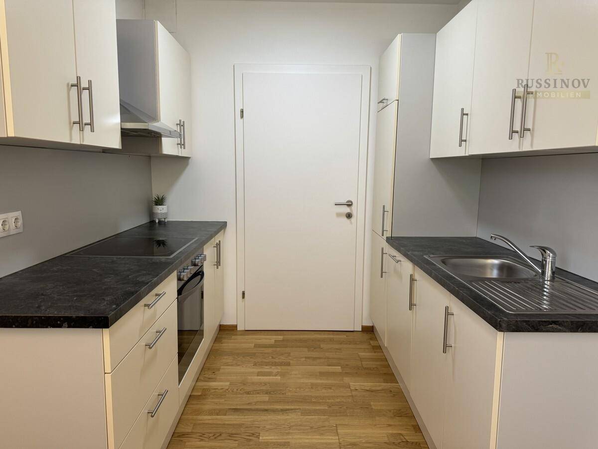 Moderne Einbauküche mit weißen Schränken, dunkler Arbeitsplatte und integrierten Geräten.