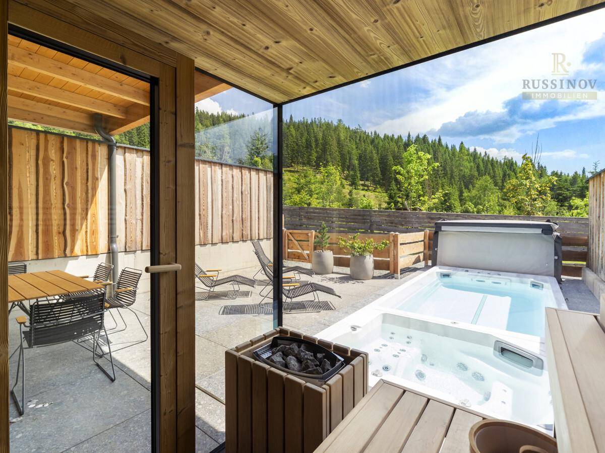 Blick von innen auf die private Terrasse mit Whirlpool, Essbereich und gemütlicher Feuerstelle im Freien.