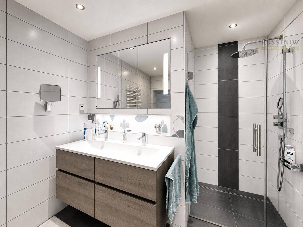 Modernes Badezimmer mit großer Dusche, Doppelwaschbecken und Spiegelschrank in hellen Grautönen.