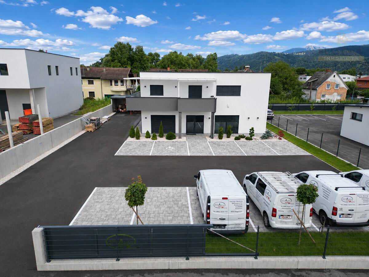 Gesamtansicht eines modernen Geschäftsgebäudes mit Parkplätzen und umliegender grüner Landschaft.