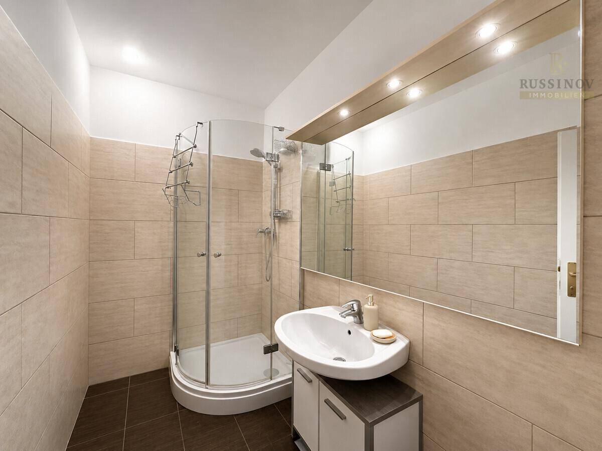 Modern gefliestes Badezimmer mit Duschkabine, Waschbecken und großem Spiegel mit Beleuchtung.