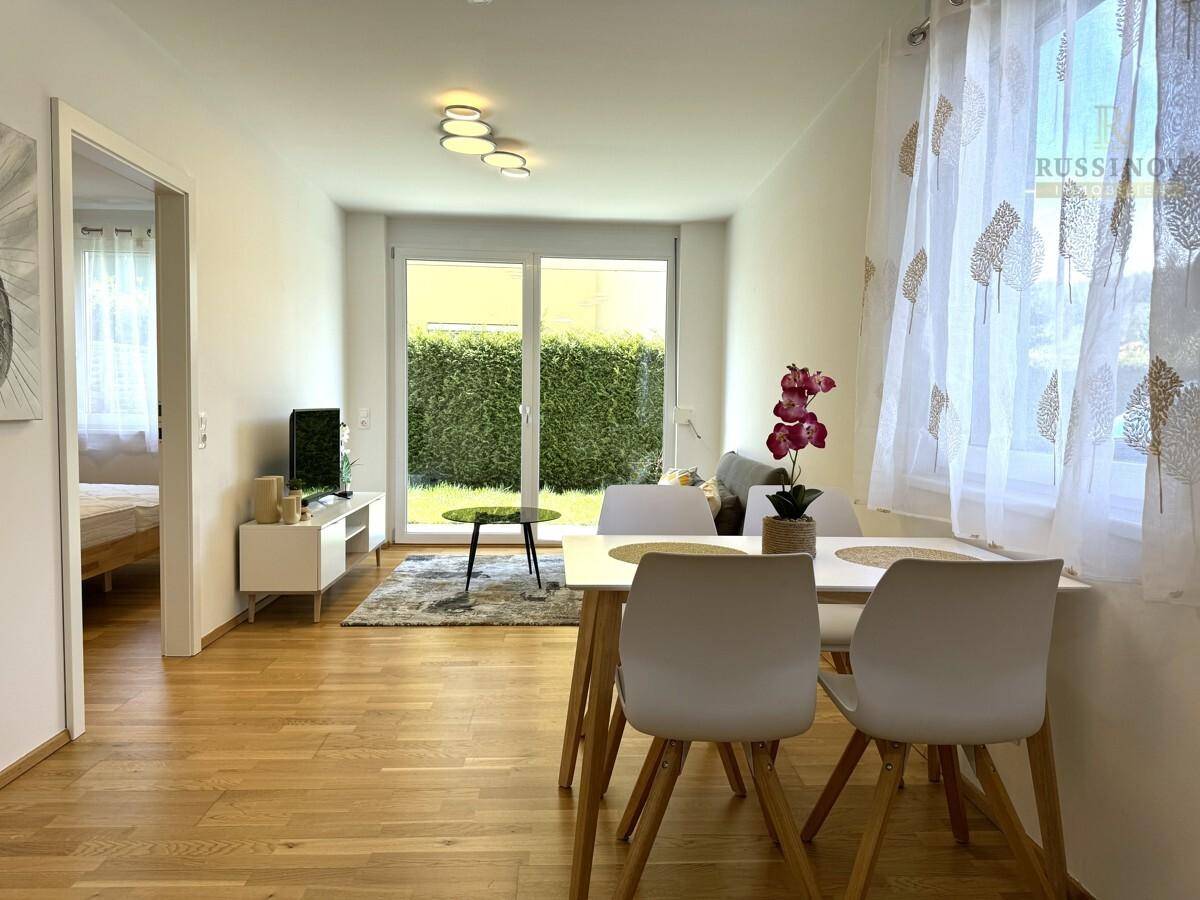 Heller Wohnbereich mit Essplatz, Holzboden und Blick auf den Garten durch große Fenster.