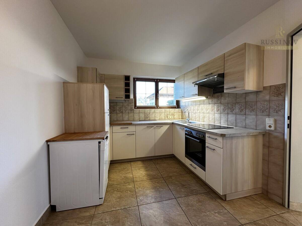 Funktionale Küche mit hellen Holzfronten, Fliesenboden und Fenster für natürliches Licht.