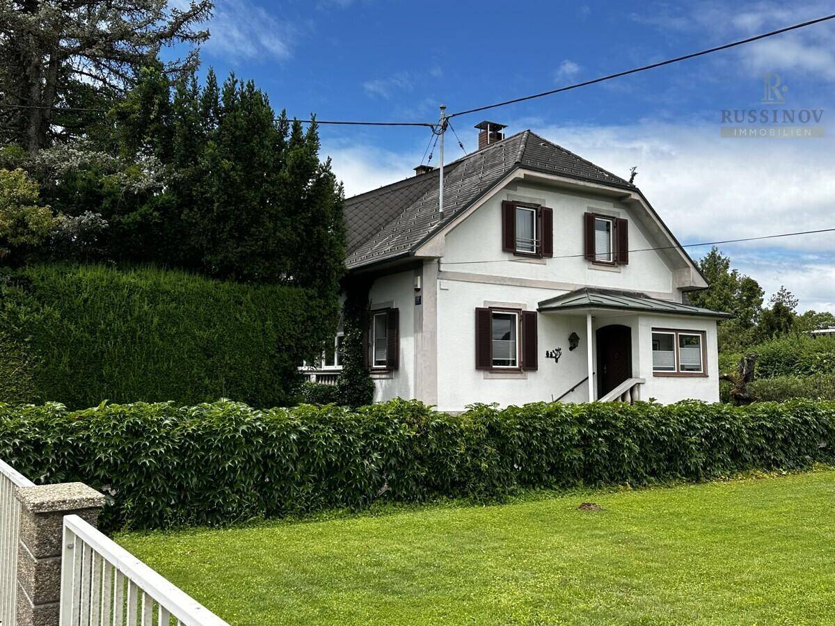 Charmantes Einfamilienhaus mit Satteldach, umgeben von gepflegtem Rasen und hohen Hecken.