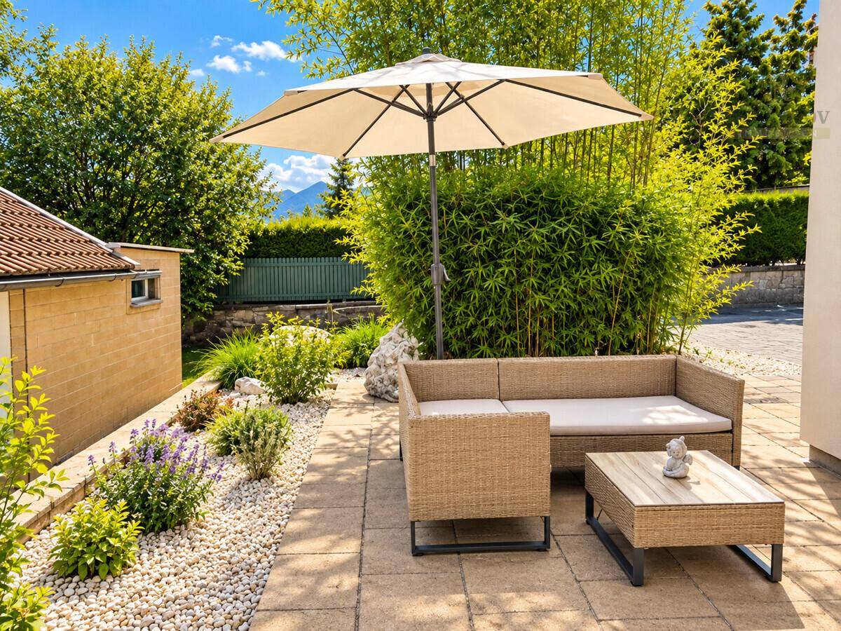 Gemütliche Terrasse mit Rattanmöbeln, Sonnenschirm und üppiger Bepflanzung.