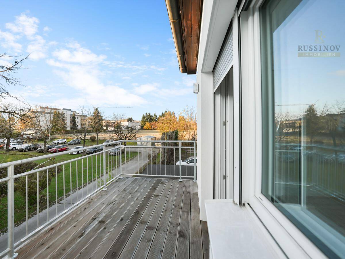 Geräumiger Balkon mit Holzboden und Metallgeländer, bietet einen Blick auf die Umgebung und Parkplätze.