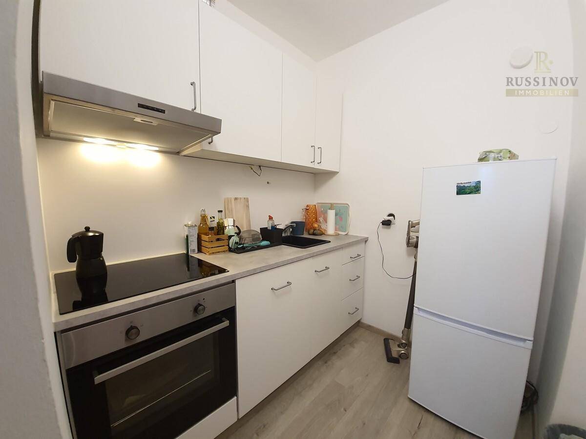 Kleine, funktionale Küche mit weißen Schränken, Herd, Backofen und Kühlschrank.