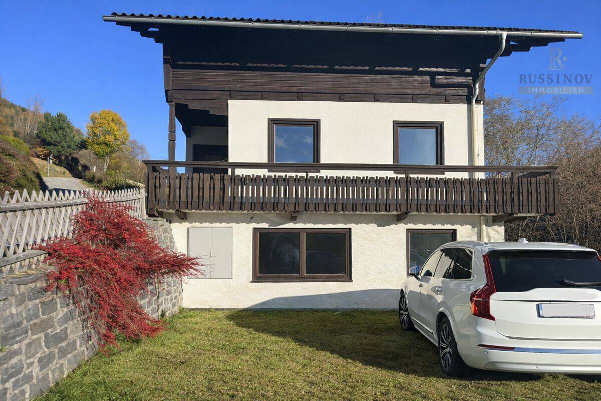 Fassade des Hauses mit einem Holzbalkon und einem geparkten Auto im Vorgarten.