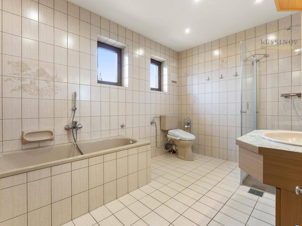 Geräumiges Badezimmer mit Badewanne, Duschkabine und beigen Fliesen.
