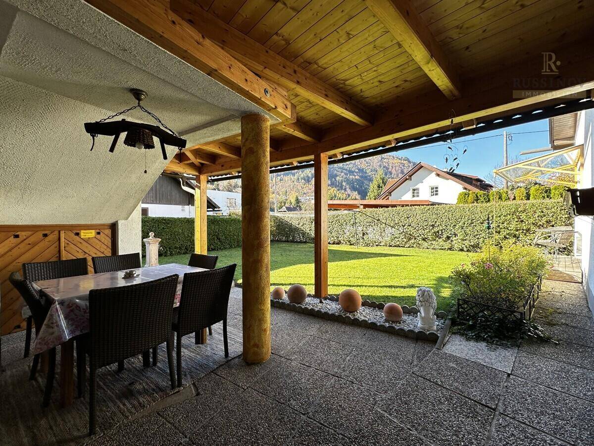 Gemütliche überdachte Terrasse mit Esstisch und Stühlen, umgeben von einem grünen Garten.