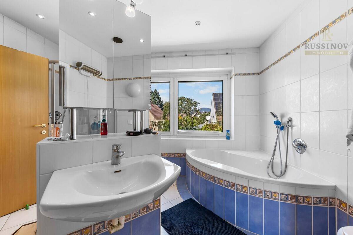 Badezimmer mit blauen und weißen Fliesen, Eckbadewanne, Dusche und Fenster für Tageslicht.