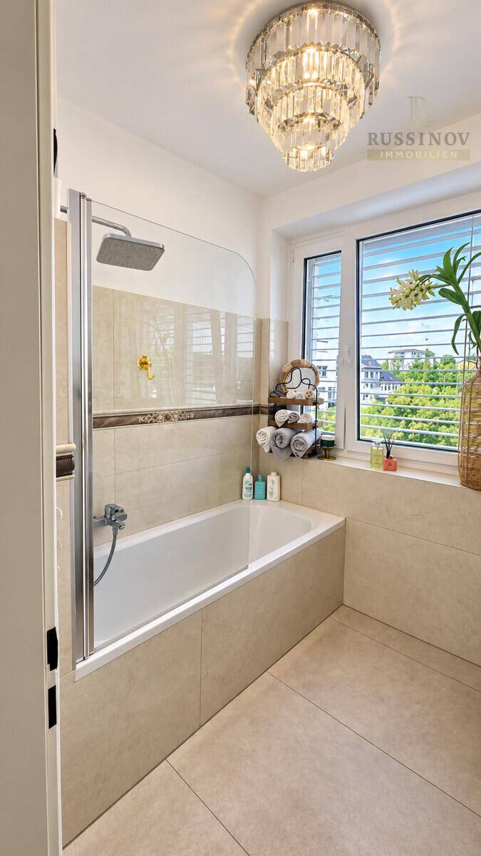 Modernes Badezimmer mit Badewanne, integrierter Dusche und großem Fenster für Tageslicht.