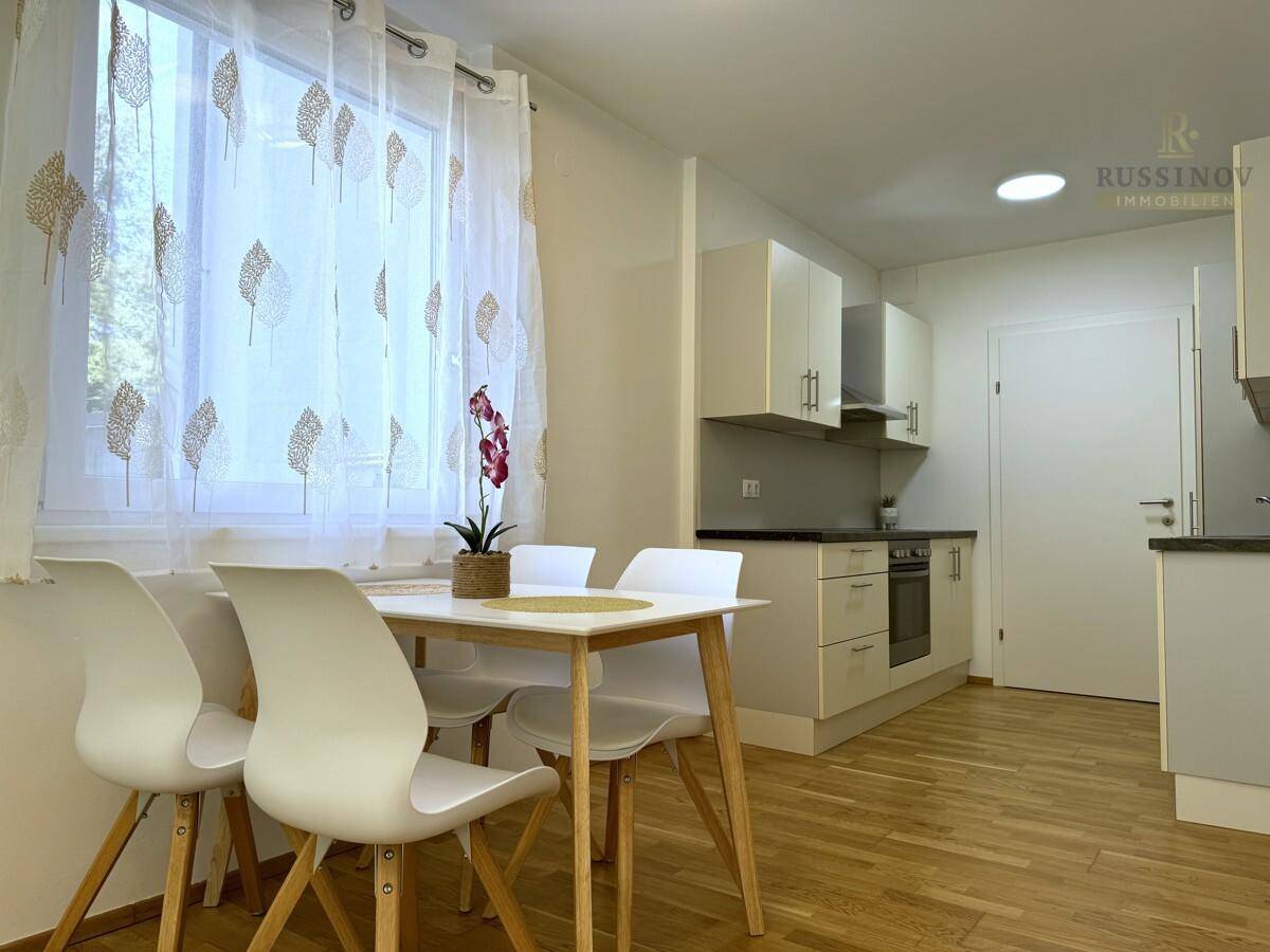 Essbereich mit Holzboden und Blick auf die moderne Küche mit weißen Schränken.