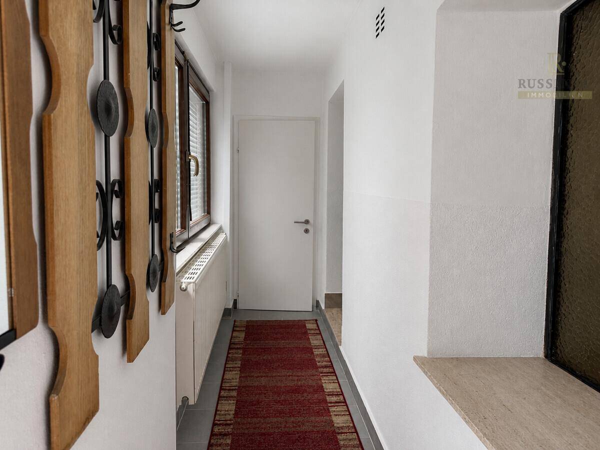 Heller Flur mit weiß gestrichenen Wänden, rotem Läufer und praktischer Garderobe.