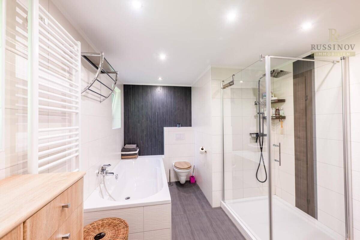 Modernes Badezimmer mit Badewanne, Dusche, beheiztem Handtuchhalter und dunkler Akzentwand.