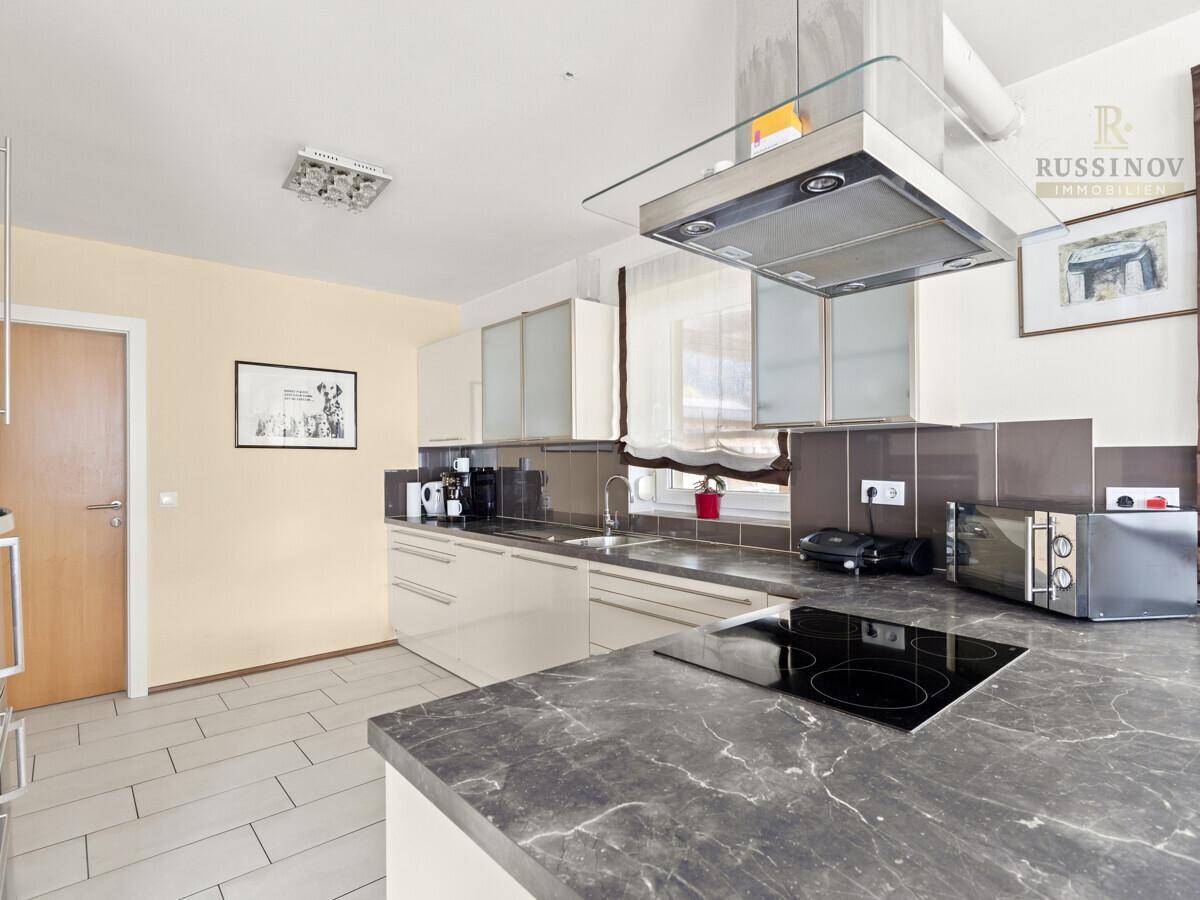 Funktionale Küche mit modernen grauen Arbeitsplatten, hellen Schränken und Fliesenboden.