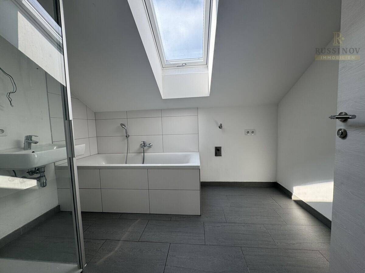 Helles Badezimmer im Dachgeschoss mit Badewanne, Dusche, Waschbecken und großem Dachfenster.