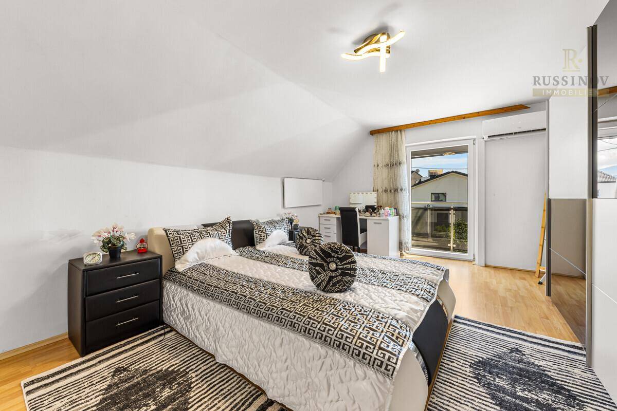 Helles Schlafzimmer im Dachgeschoss mit Balkonzugang, Schreibtisch und Holzboden.