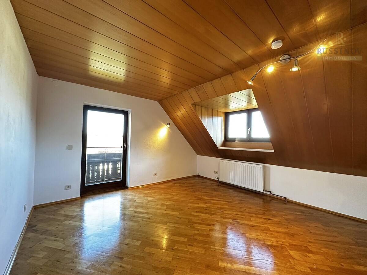 Geräumiges Zimmer mit Holzboden, Dachschräge und Zugang zu einem kleinen Balkon.