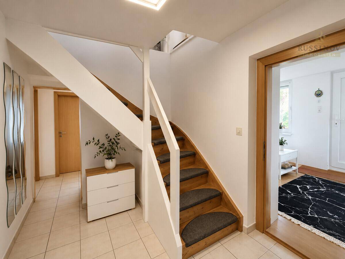 Heller Flur mit Treppe, Fliesenboden und einem modernen Sideboard, das zum Obergeschoss führt.
